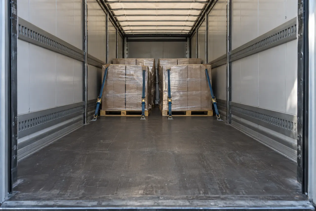Interior de un tráiler cargado a medias con palets bien trincados y luz natural entrando por las puertas.